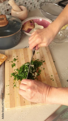 Anonymous person chops parsley and garlic on kitchen table at home. Healthy eating and traditional cuisine. Seasonal farm products.