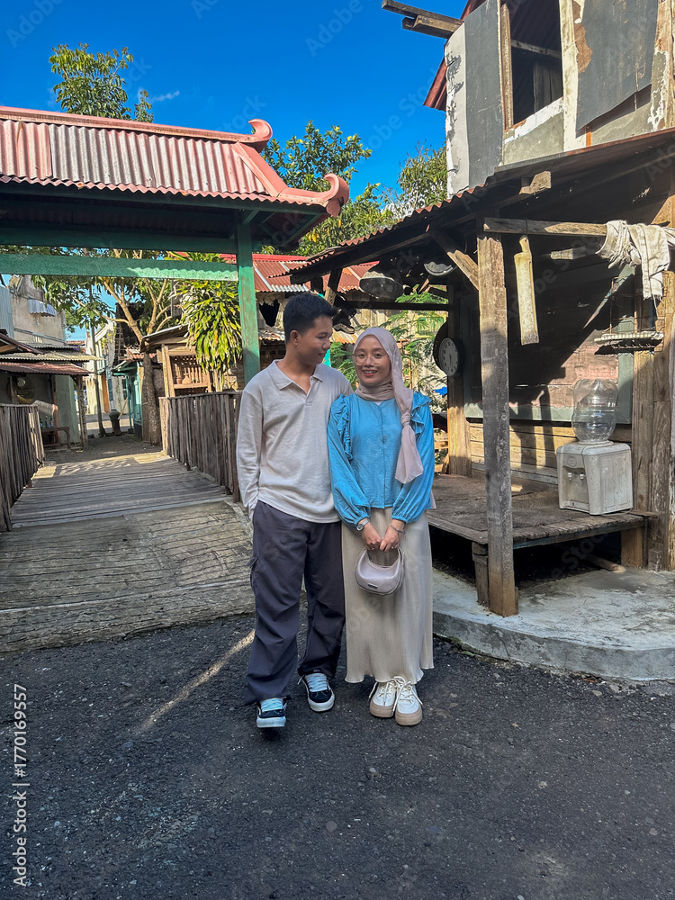 Obraz premium A couple stands side by side in a charming village, smiling under the bright blue sky
