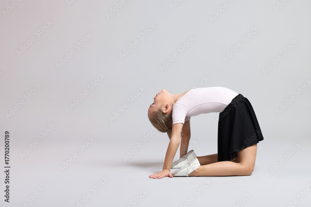 Naklejka premium Cute little girl doing gymnastic exercise on grey background. Space for text
