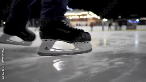 Close-up slow motion footage of a person ice skating on a rink at night with a blurry background
