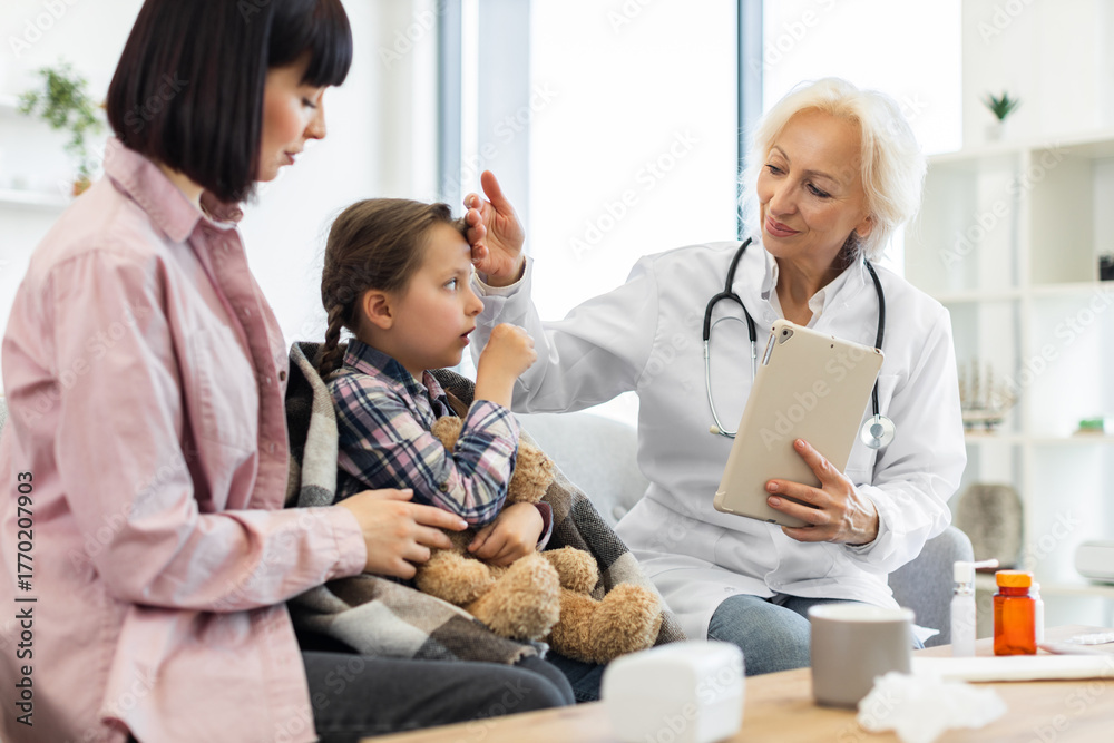 Obraz premium A young girl with a cold is being examined by a doctor while her mother comforts her. The doctor is checking the child's temperature with a tablet in hand.