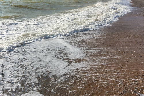Turquoise sea in close-up in bright sunlight. Colorful tropical background. The concept of summer vacation, travel. Clear blue water, small waves lapping at the sandy shore. The texture of the beach