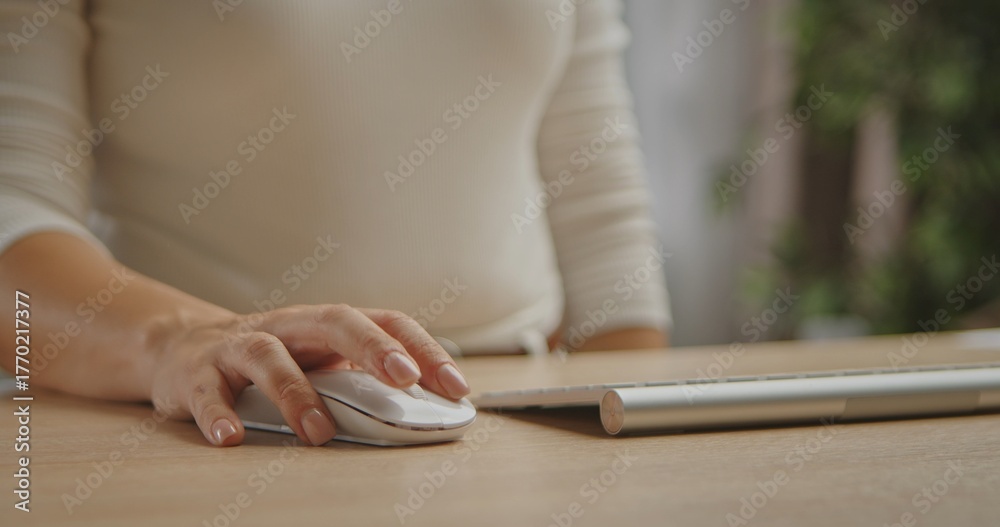 Fototapeta premium A woman hand operating a wireless mouse on a wooden desk next to a modern keyboard. Ideal for illustrating tech and productivity concepts.