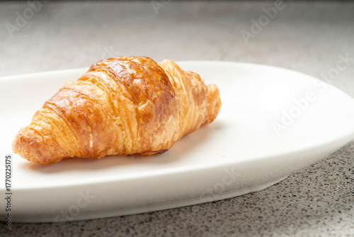 Croissant with flaky pastry showing layers of baked dough on a simple white plate
