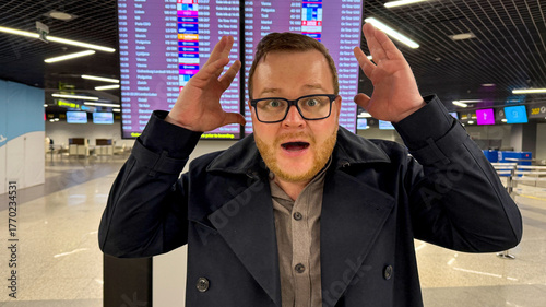 Фотография A bewildered Caucasian man in glasses exclaims at the chaotic flight display, ca