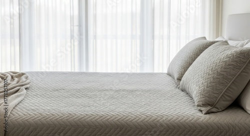 Comfortable bed with textured bedding and pillows against a bright window