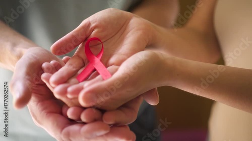 Female and male hands gently hold a red ribbon. Symbol of AIDS awareness, HIV prevention, support, protection and global compassion during awareness month.