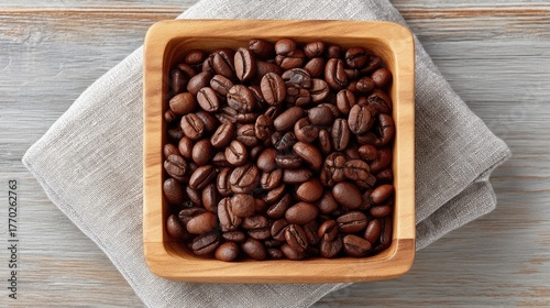 A Styled Flat Lay Of Roasted Coffee Beans Scattered In A Square Wooden Bowl On A Textured Napkin And Wooden Surface In Natural Light