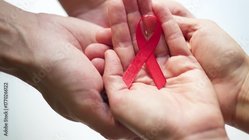 Man's hand passing red satin ribbon to woman's hand symbolizing shared commitment to HIV AIDS awareness and December solidarity.