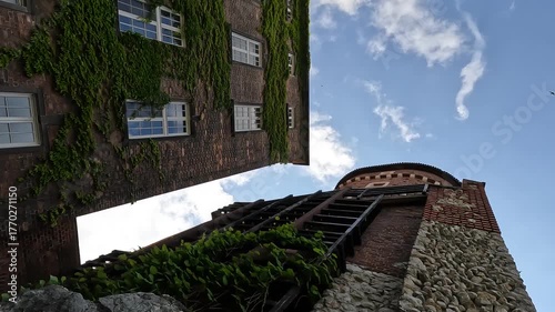 Low angle view of an ivy-covered tower at Wawel Castle in Krakow, Poland - green vines climbing historic stone architecture on a cloudy summer day .