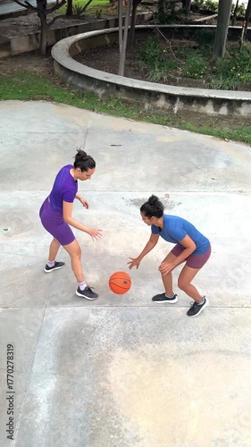 Two young female athletes competing in a game of one on one basketball on an outdoor court