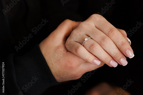 Romantic Engagement: Hands Holding Diamond Ring, Couple, Love, Proposal, White Gold, Close-up, Black Background, Intimate Moment, Celebration.
