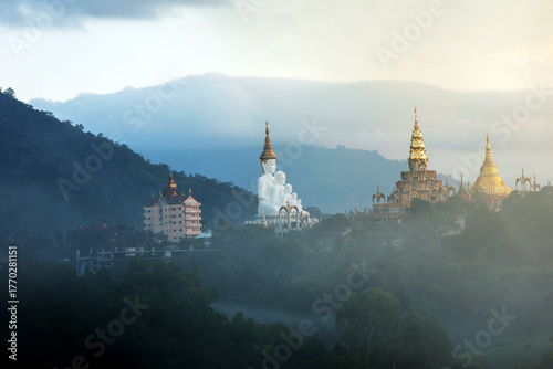 The stunning scenery of Wat Phra That Pha Sorn Kaew in Thailand showcases five serene Buddha statues and a golden pagoda surrounded by lush green hills, morning mist, and a glowing sunrise sky.