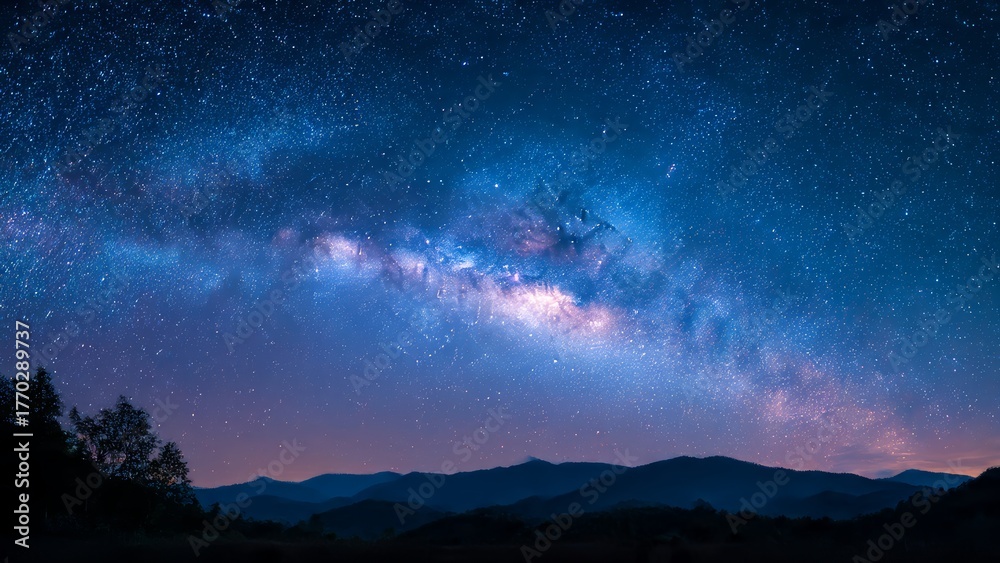 Fototapeta premium Starry night sky over silhouetted mountains and trees showcasing the Milky Way galaxy