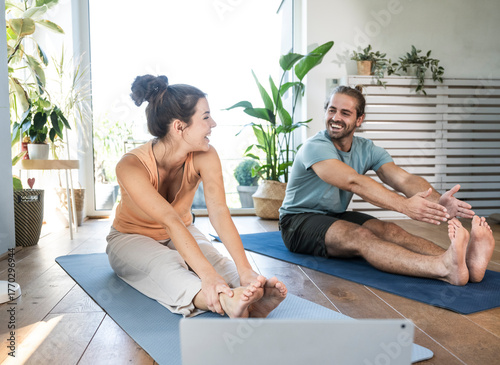 Happy young couple practicing stretching exercise on mats at home
