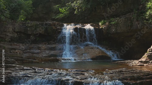 Sunlight hits St. Mary's Falls as it cascades over a rocky ledge into a tranquil pool. Filmed on a summer morning in St. Mary's Wilderness, Virginia (George Washington NF).