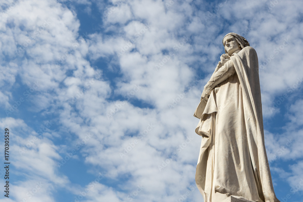 Fototapeta premium The Dante Alighieri statue in central Verona, standing against a cloudy blue sky, honoring the famous poet and reflecting the historic and cultural heritage of Italy
