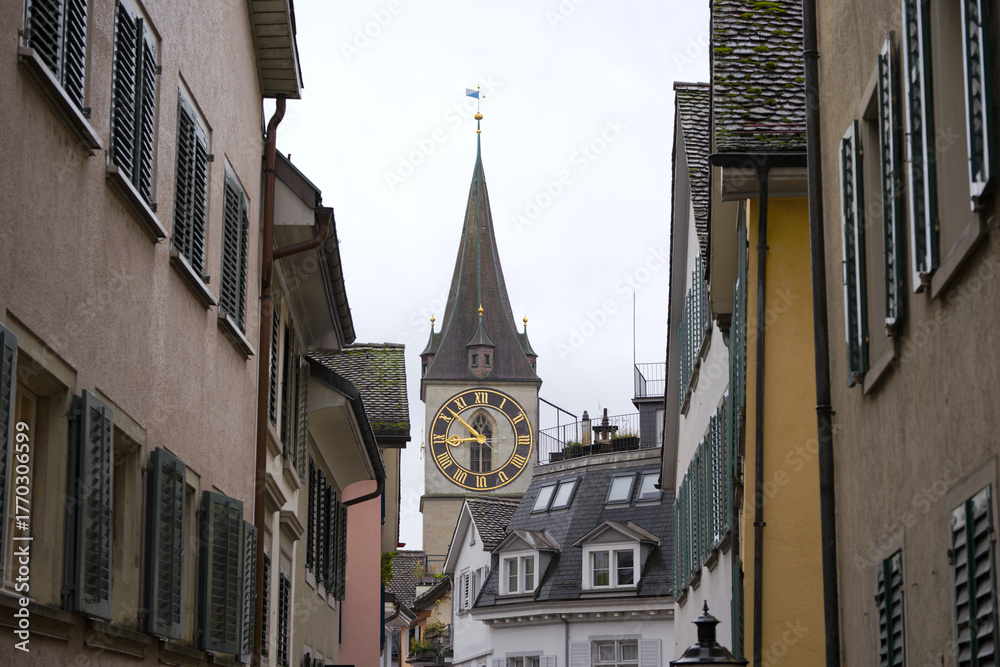Fototapeta premium Citycape with alley and church tower with clock face of Saint Peter church at the old town of Swiss city of Zürich on cloudy and rainy autumn day. Photo taken October 27th, 2025, Zurich, Switzerland.