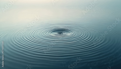 Water surface shows circle wave ripple pattern. Fluid dynamic motion reveals smooth surface. Water drop causes flow. Rings radiate outwards on liquid. Great for background design with calmness.
