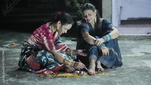 Two Indian women applying aalta (a traditional red dye) on their feet before Hindu puja and festival celebration