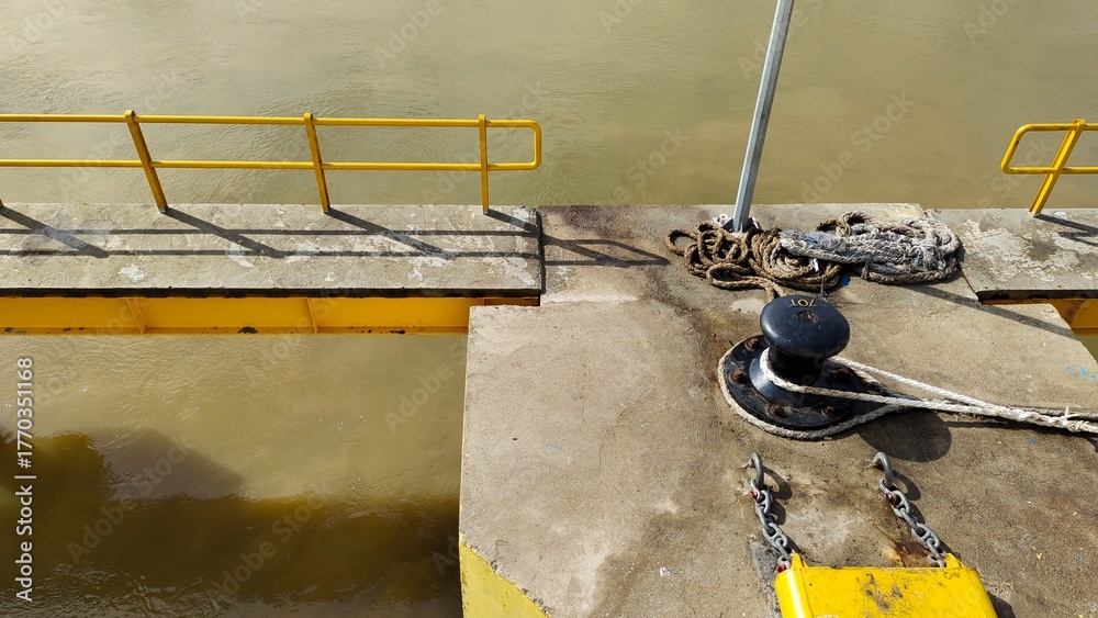 Fototapeta premium Yellow Dock Pier with Ropes and Bollard by the River Edge