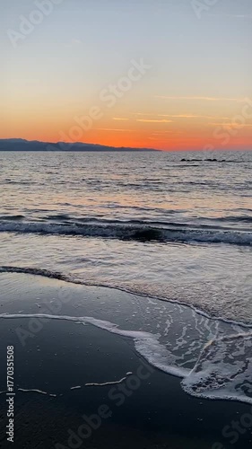 Sunset on calm ocean shore with gentle waves and orange-tinted sky, perfect for background