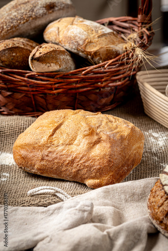 Fresh homemade bread in wicker basket on burlap background with grains