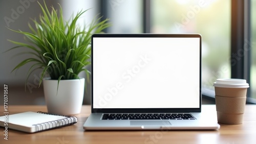 Blank laptop screen on wooden desk beside green plant notebook and takeaway coffee cup with copyspace in sunlit office, concept of remote work, digital marketing, freelance productivity