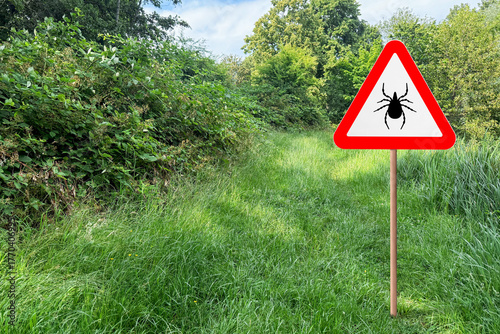 Foto Warning sign marking habitat of ticks in nature