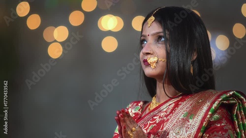 A newly married Hindu woman dressed in a red saree with traditional ornaments folds her hands in namaskar. The soft bokeh background highlights her calm and graceful expression.