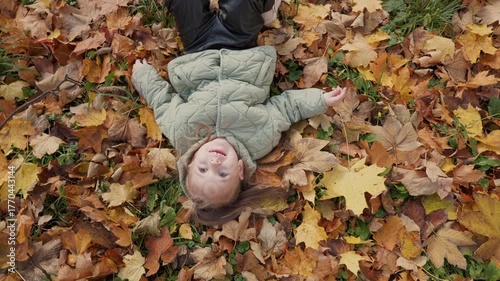 A cheerful child lies on autumn leaves. An active child girl plays on an autumn day in the park.