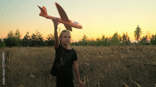 Child aviator with airplane dreams of traveling in summer in nature at sunset. Girl with plane on meadow. Summer leisure.