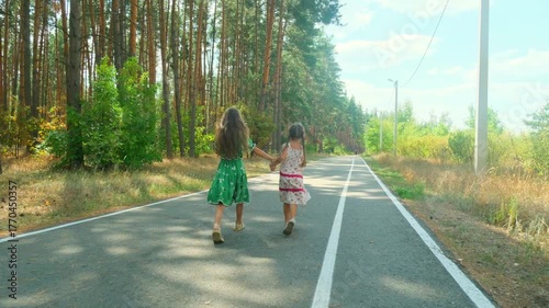 Two happy child girls running in the forest in summer. Sisters relaxing in nature in the park