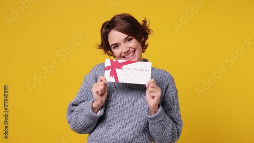 Young woman wear grey knitted sweater white shirt casual clothes pointing finger on gift certificate coupon voucher card for store show thumb up isolated on plain yellow background. Lifestyle concept
