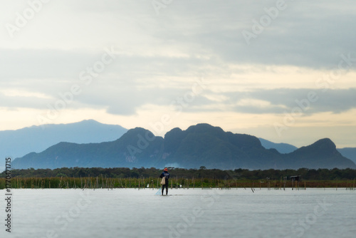 Local fisherman working in the lake with mountain view in southern Thailand during sunrise, peaceful rural lifestyle and natural landscape.
