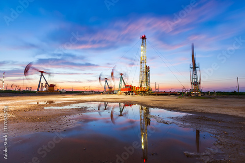 in the evening, oil pumps are running, The oil pump and the beautiful sunset reflected in the water, the silhouette of the beam pumping unit in the evening.