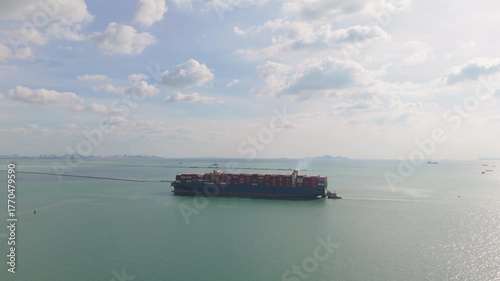 Aerial view of a large cargo container ship sailing in the ocean near an industrial port in Thailand