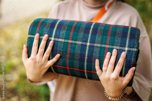 Person holding folded tartan picnic blanket outdoors