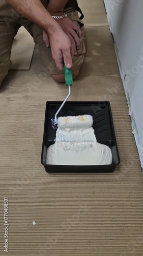 4K close-up video showing a person covering a paint roller with white glue before use, in workshop lighting.