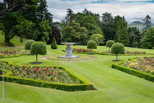 Scenic summertime view of an attractive English style landscape garden with a fresh mowed grass lawn, green leafy trees and topiary hedge - garden and nature themed photograph.