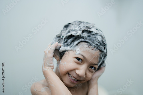 A smiling child covered in shampoo foam enjoying bath time while washing hair, showing fun and clean hygiene habits.