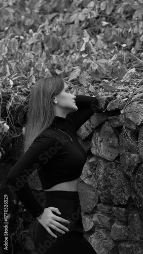 A woman in a black crop top and wide-leg pants stands by a stone wall on the steps in a park. She has her head thrown back and is relaxedly breathing in the fresh air, enjoying a moment of peace.