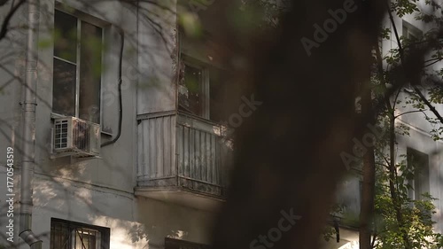 View of the facade and balcony of a five-story building through the leaves
