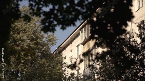 View of the facade and balcony of a five-story building through the leaves