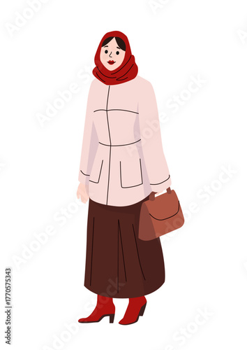 Woman in long brown skirt and pink jacket with red headscarf and boots holding handbag dressed for winter weather