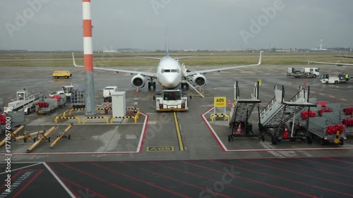 Parked jet, Cloudy airport, Terminal equipment. Cloudy day sees airplane at gate, attended by ground support and equipment.