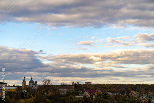 Small town with residential houses and church with domes under cloudy sky at sunset. Landscape photography with wide horizon and copy space. 