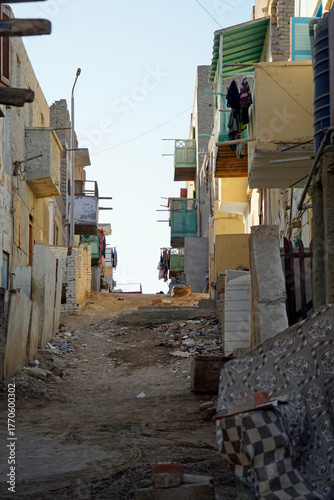 Narrow, dirty dirt road between crumbling multi-story buildings