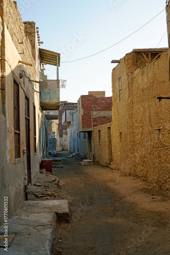 Narrow, dirty dirt road between crumbling multi-story buildings