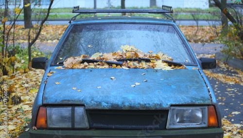 An old blue, dirty car is covered in fallen yellow leaves, Iskrovsky Prospekt, Saint Petersburg, Russia, October 26, 2025